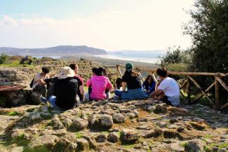 students sit on an archaeological site with view of the sea